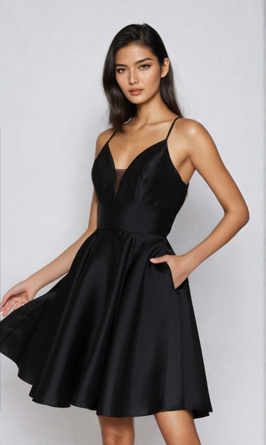 A woman wears the Lace-Back Short A-Line Homecoming Dress 8698—a sleeveless black cocktail dress with thin straps, fitted bodice, and flared skirt—posing against a light background. An elegant choice for any special occasion.
